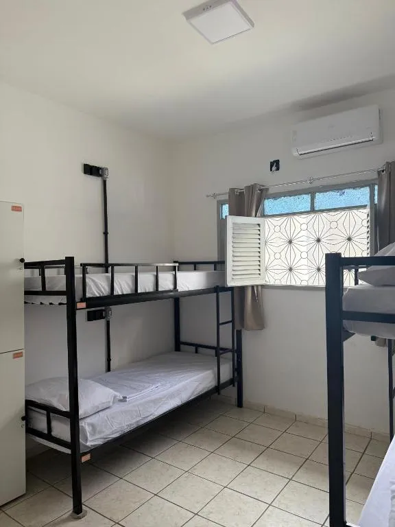 Dormitório feminino com dois beliches de metal preto, armário e janela com grade decorativa