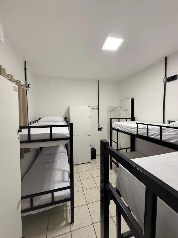 Dormitório feminino com beliches de metal preto, armário branco e piso de cerâmica