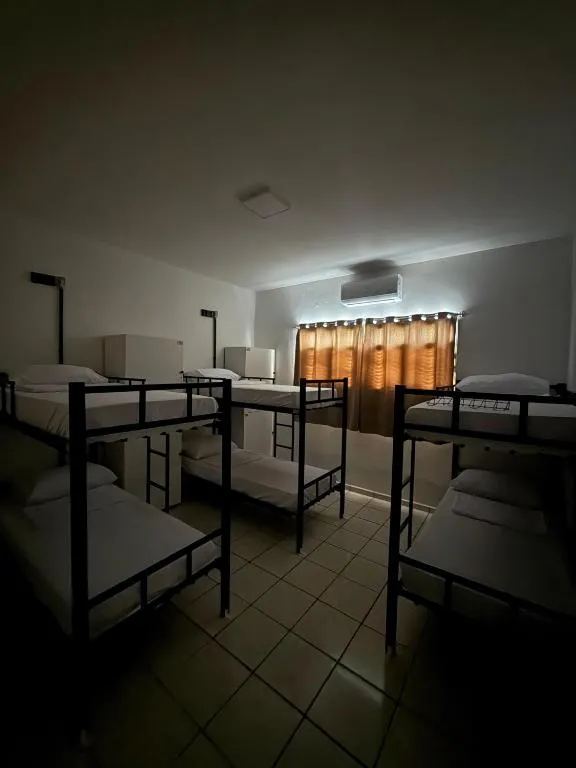 Dormitório misto com três beliches de metal e cortinas separando as camas