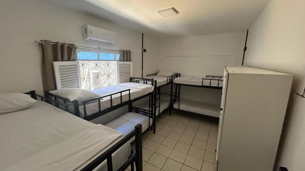Dormitório misto amplo com cama de solteiro e beliches, armário branco e janela com persiana