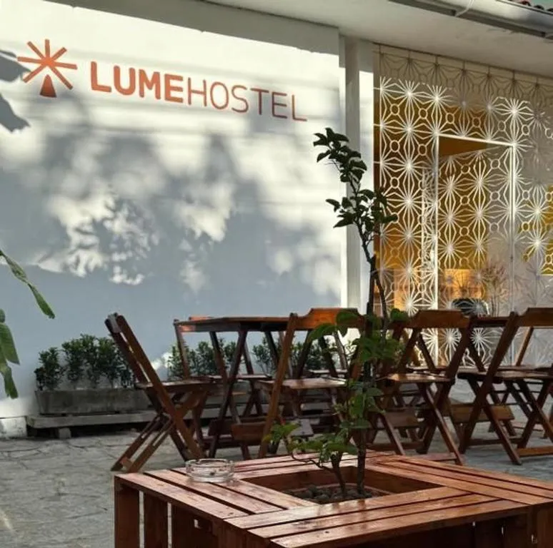 Pátio de entrada do LumeHostel com mesas de madeira e a fachada com o logo ao fundo