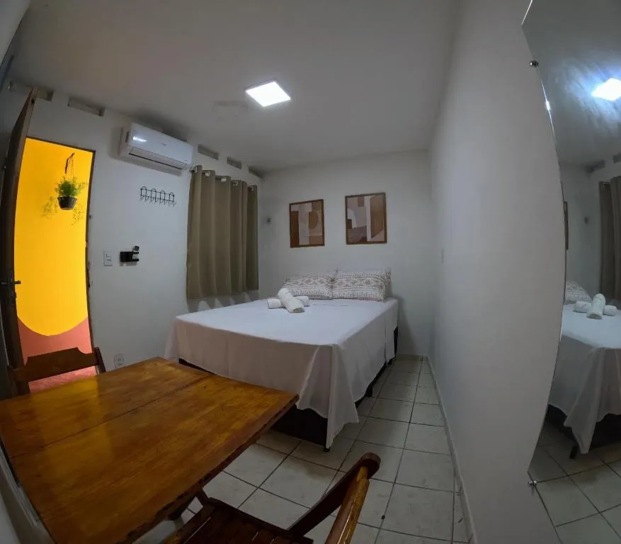 Suíte privativa com cama de casal, mesa de madeira, cadeiras e espelho de corpo inteiro