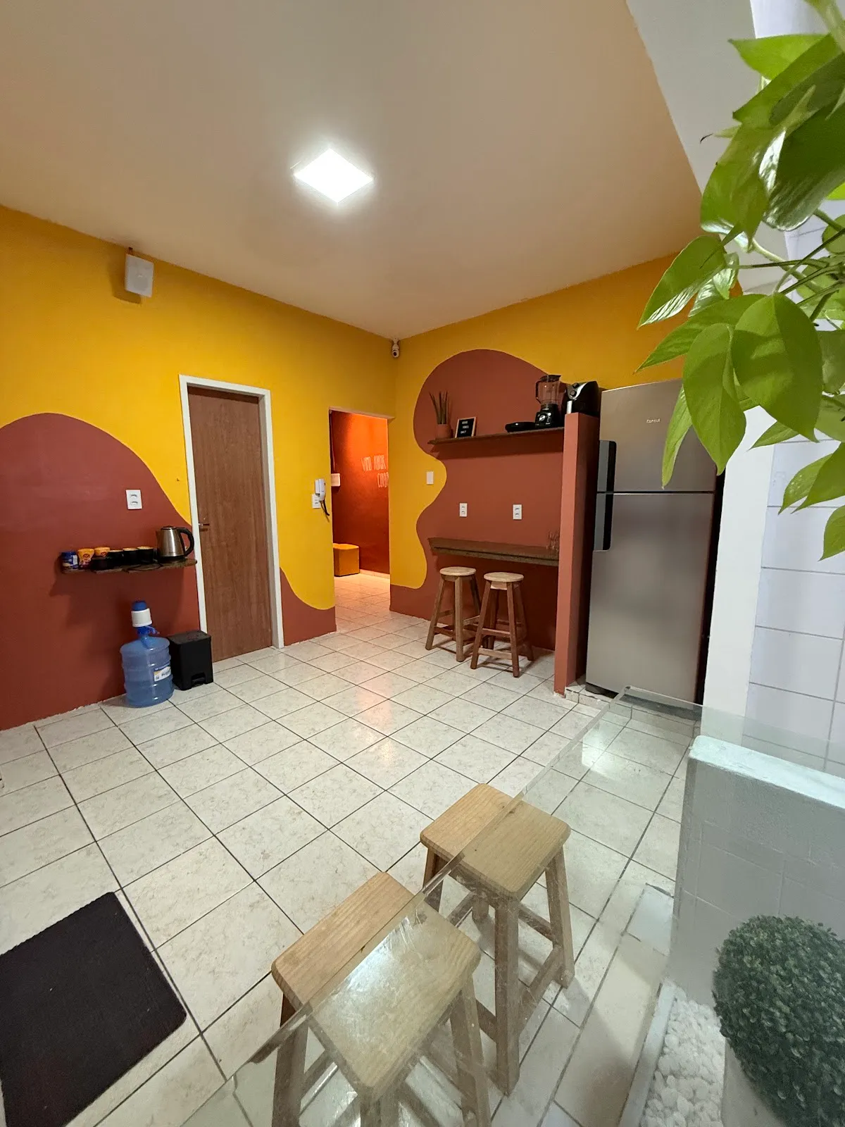 Corredor interno do LumeHostel com paredes amarela e terracota, geladeira e balcão com banquinhos
