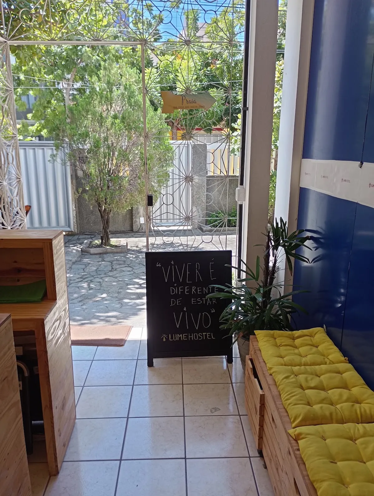 Espaço de estar próximo à entrada do LumeHostel, com almofadas amarelas e quadro com frase inspiracional
