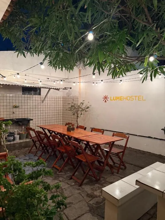 Pátio do LumeHostel à noite, com mesa comunitária e varal de luzes